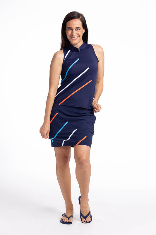 Full front view of a smiling woman wearing the Straight Drive Sleeveless Golf Top in Navy Blue and the Straight Drive Golf Skort in Navy Blue. This is a solid navy blue top with four diagonal lines from approximately the middle front of the top down to th