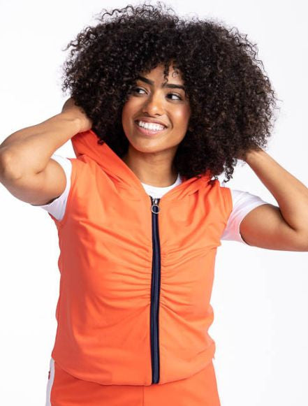 Close front view of a smiling woman wearing the Fall Ball Golf Vest in Coral Red. This is a solid coral red vest with a black front zipper and elastic waistband.