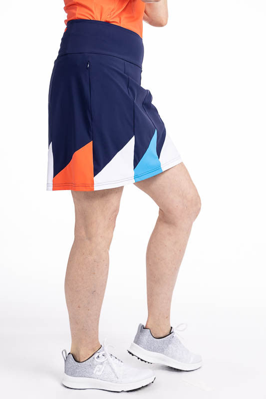 Right side view of the Helping Wind Golf Skort in Navy Blue. This is a navy blue skort with alternating triangles shaped like golf flags of white, pacific blue and coral red around the hemline. It features two in-seam pockets and a built-in medium grey sh