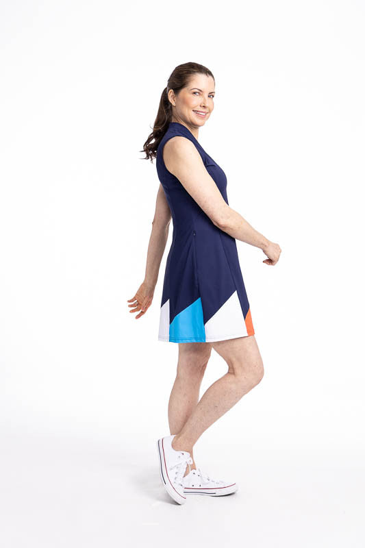 Full right side view of the Helping Wind Sleeveless Golf Dress in Navy Blue. This is a solid navy blue dress with alternating triangles shaped like golf flags in white, pacific blue, and coral red around the hemline. It also features two side pockets and 