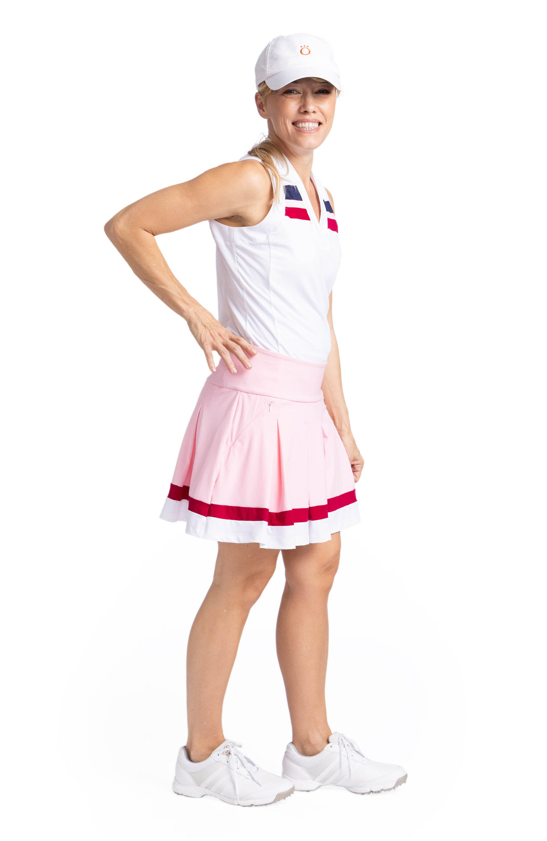 Side view of a woman wearing a white, V-neck, sleeveless top with contrasting navy blue, Bordeaux Red, and white stripes on the upper chest. She is also wearing the Whirl and Twirl Skort in Ballet Pink. 