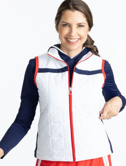 Smiling woman wearing the Chill Layer Golf Vest in White. This vest is primarily white, with a solid, horizontal navy blue stripe across the front and back of this vest. There are also tomato red accents on either side of the zipper on the front and aroun