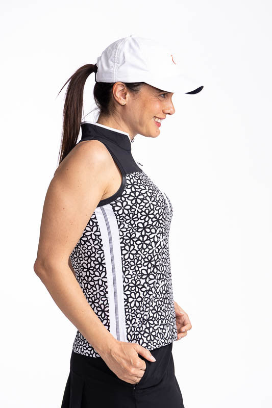 Right side view of a woman wearing the Resolution Sleeveless Golf Top in Fall Bloom print and the We've Got You Covered Hat in White. This top consists of a black yoke, fall bloom print on the bodice, a white stripe with black stitching on each side, and 