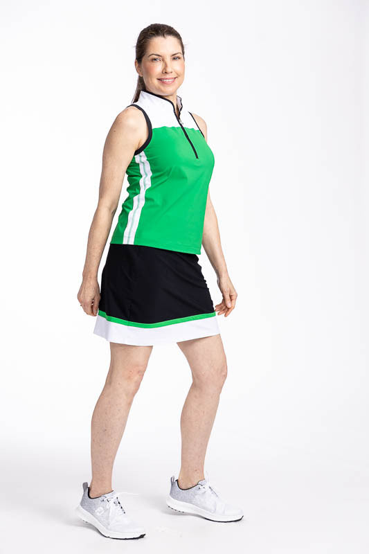 Full right side view of a smiling woman wearing the Resolution Sleeveless Golf Top in Rye Grass Green and the In Play Golf Skort in Black/Green. This top has a white yoke, rye grass green body, a white stripe down each side and black trim around the colla
