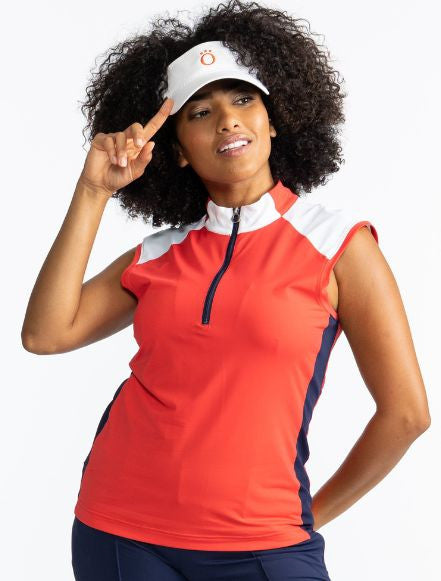 Smiling woman wearing the Cap to Tap Short Sleeve Golf Top in Tomato Red and the No Hat Hair Visor in White. This top has solid white triangles on each shoulder, solid white sections on either side of the front of the collar on either side of the zipper, 