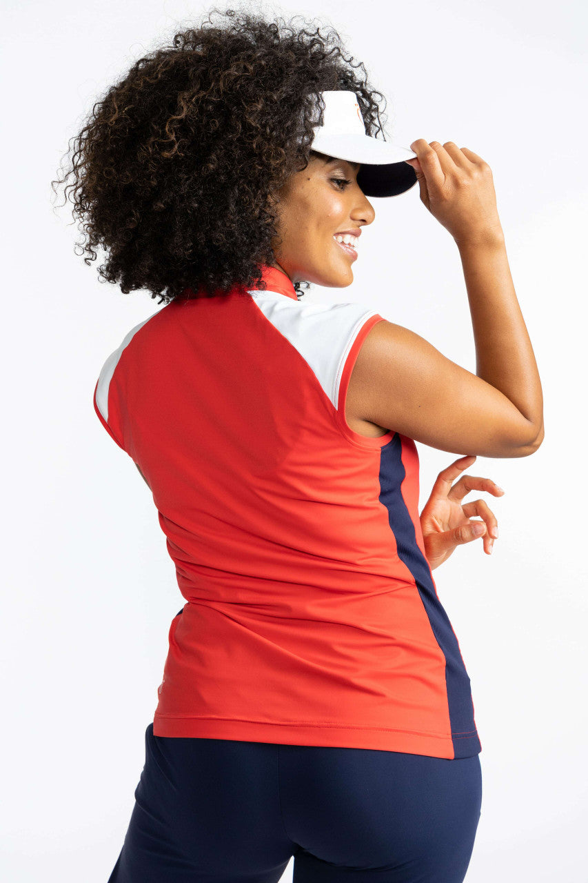 Back view of the Cap to Tap Short Sleeve Golf Top in Tomato Red and the No Hat Hair Visor in White. This top has solid white triangles on each shoulder, solid white sections on either side of the front of the collar on either side of the zipper, a navy bl