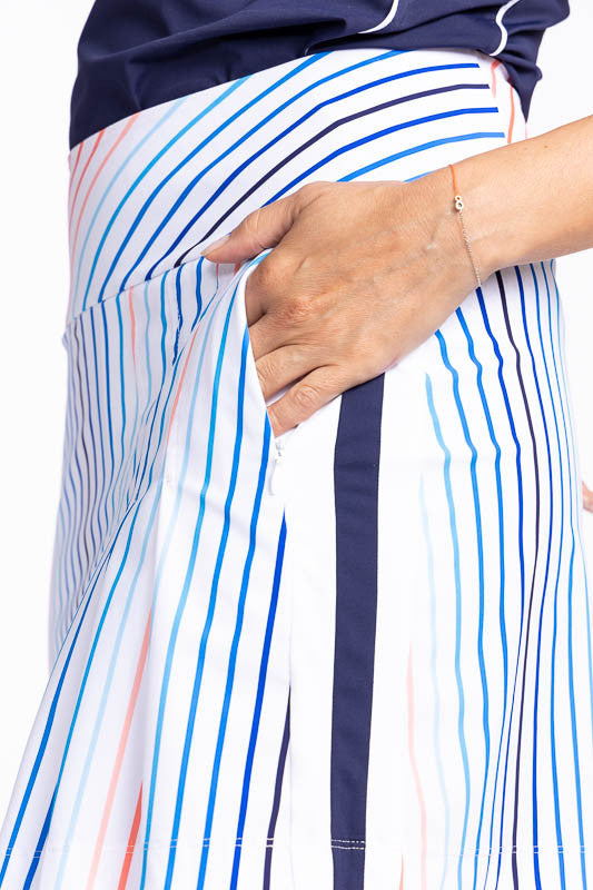 Close left side view of one of the pockets on the Party Pleat Golf Skort in Sun Stripe print. The print consists of a mix of horizontal and vertical stripes in coral red, pacific blue, and navy blue on a white background.