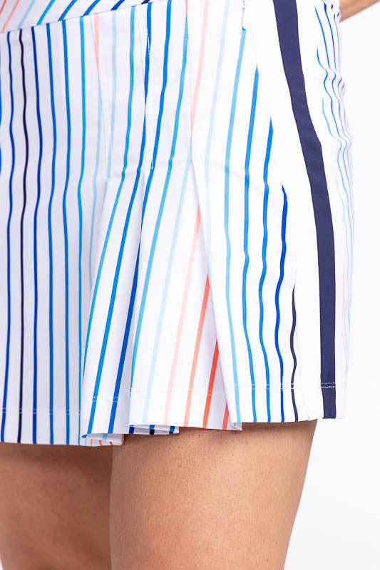 Close left side view of the hemline on the Party Pleat Golf Skort in Sun Stripe print. The print consists of a mix of horizontal and vertical stripes in coral red, pacific blue, and navy blue on a white background.