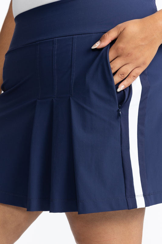 Close right side view of the pocket on the Party Pleat Golf Skort in Navy Blue. In this view, you can see one of the solid, white stripes that runs down the side of this skort.