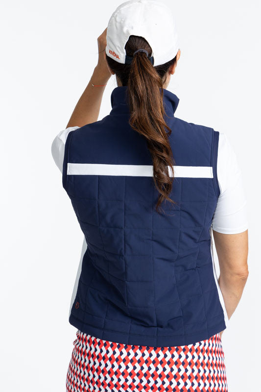 Back view of the Chill Layer Golf Vest in Navy Blue, the Tee it Up Short Sleeve Golf Top in White, and the We've Got You Covered Hat in White. There is a solid, horizontal white stripe that runs across the front and back of this vest just above the chest 