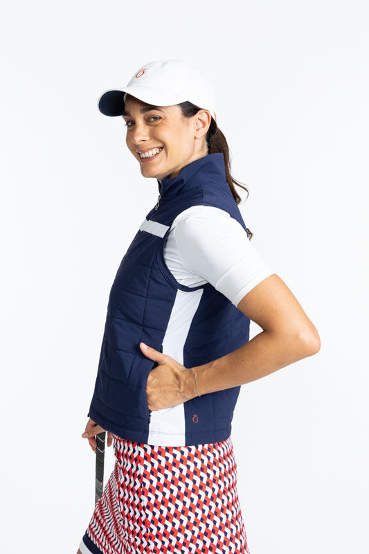 Left side view of the Chill Layer Golf Vest in Navy Blue, the Tee it Up Short Sleeve Golf Top in White, and the We've Got You Covered Hat in White. There is a solid, horizontal white stripe that runs across the front and back of this vest just above the c