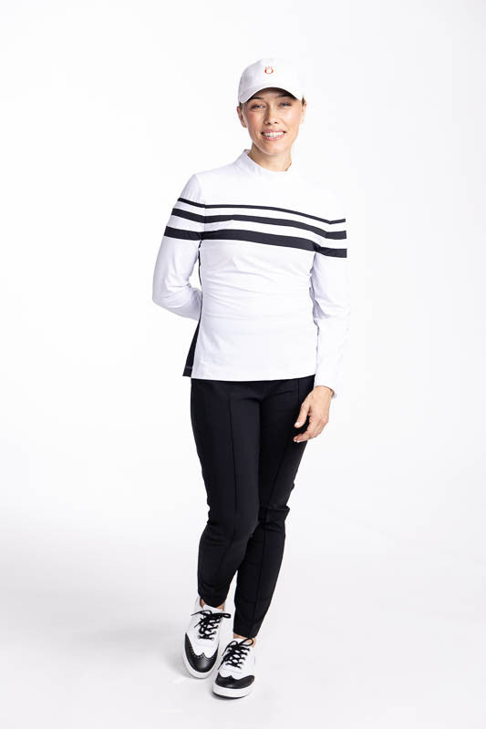 Full front view of a woman wearing the Winter Rules Long Sleeve Golf Top in White, the Tailored Crop Pants in Black, and the We've Got You Covered Hat in White. This top has three black stripes around the top and one black stripe down each side.