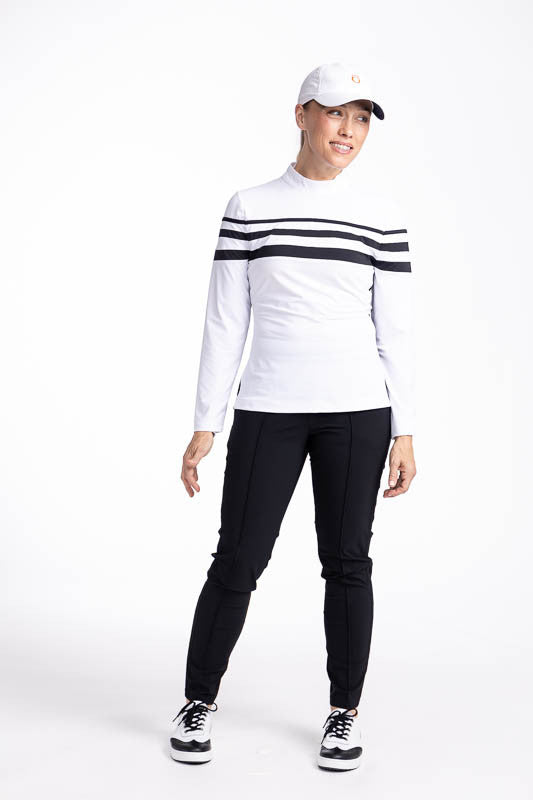 Full front view of a woman wearing the Winter Rules Long Sleeve Golf Top in White, the Tailored Crop Pants in Black, and the We've Got You Covered Hat in White. This top has three black stripes around the top and one black stripe down each side.
