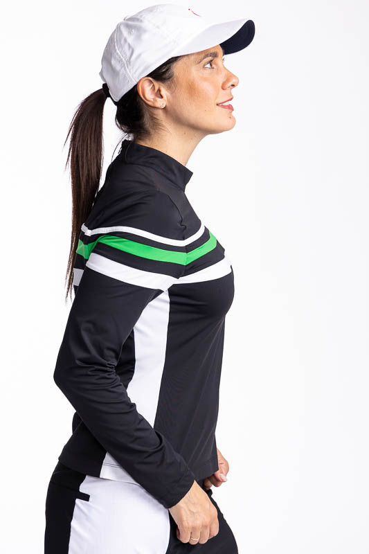 Right side view of a woman wearing the Winter Rules Long Sleeve Golf Top in Black and the We've Got You Covered Hat in White. This top features three alternating stripes of white, rye grass green, and white stripes on a black long sleeve top with one whit