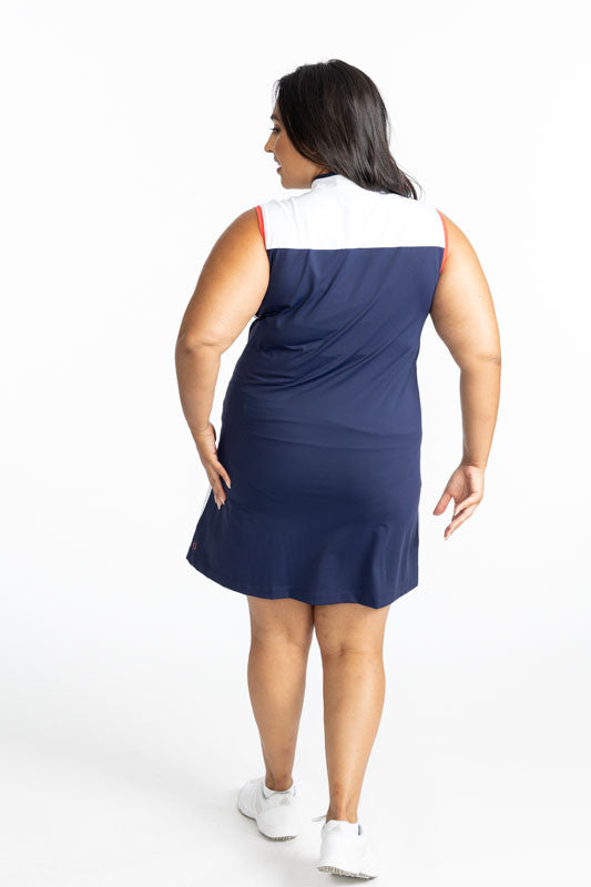 Back view of the Clubhouse Sleeveless Golf Dress in Navy Blue. This dress has white accents at the top on the front and back of this dress, a white stripe with a tomato red line down the middle of each stripe that runs down each side, and tomato red accen