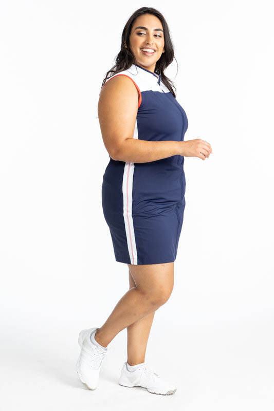 Right side view of the Clubhouse Sleeveless Golf Dress in Navy Blue. This dress has white accents at the top on the front and back of this dress, a white stripe with a tomato red line down the middle of each stripe that runs down each side, and tomato red