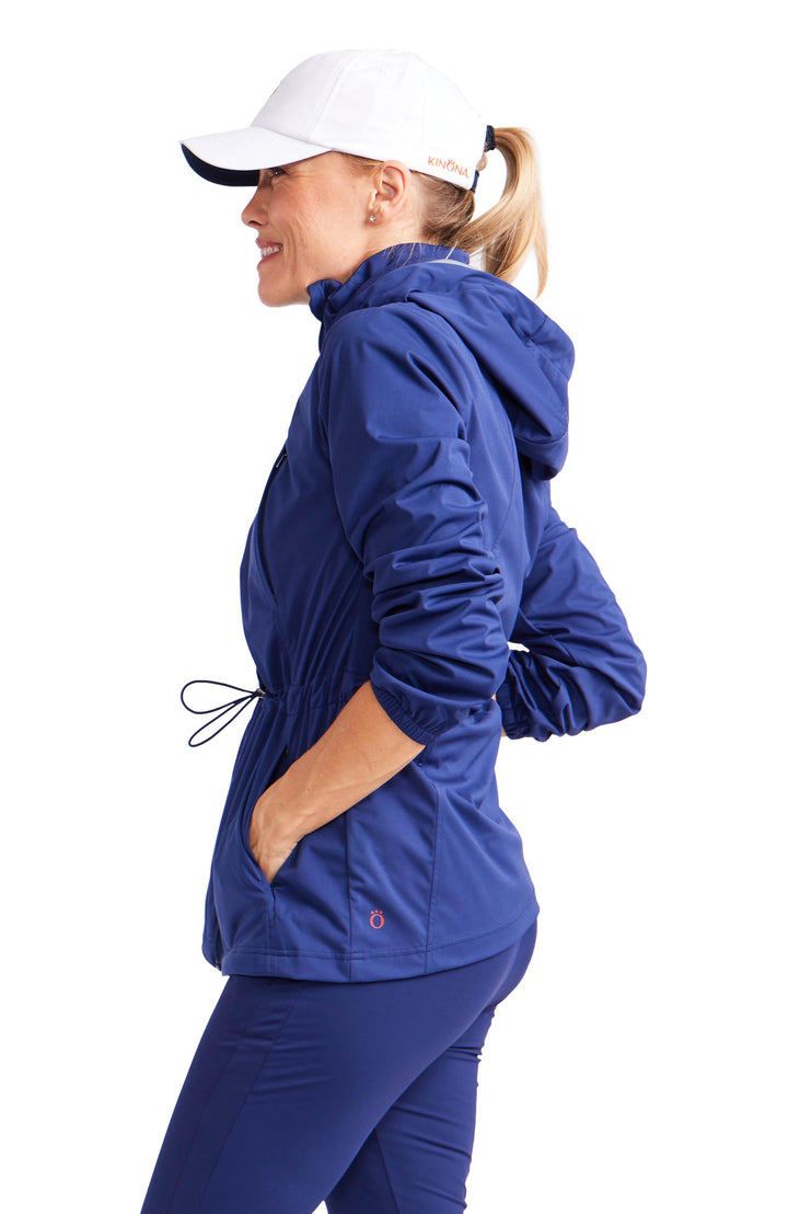 Side view of woman wearing navy blue hooded golf rain jacket with cinch waist.