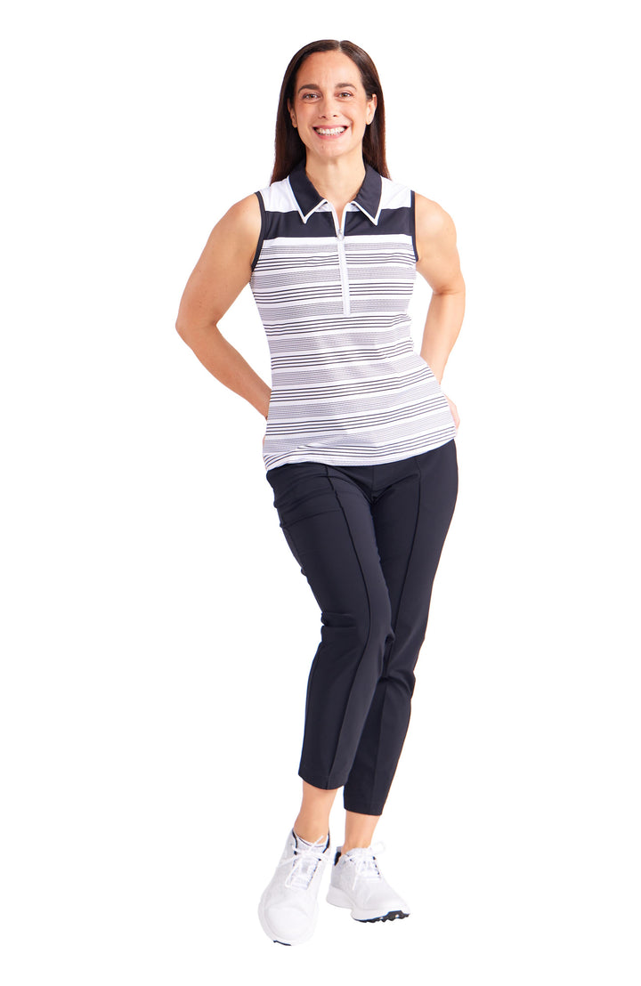 Full front view of woman wearing white with black stripe quarter zip sleeveless top with black collar and white trim. Woman wearing solid black crop pants and white tennis shoes