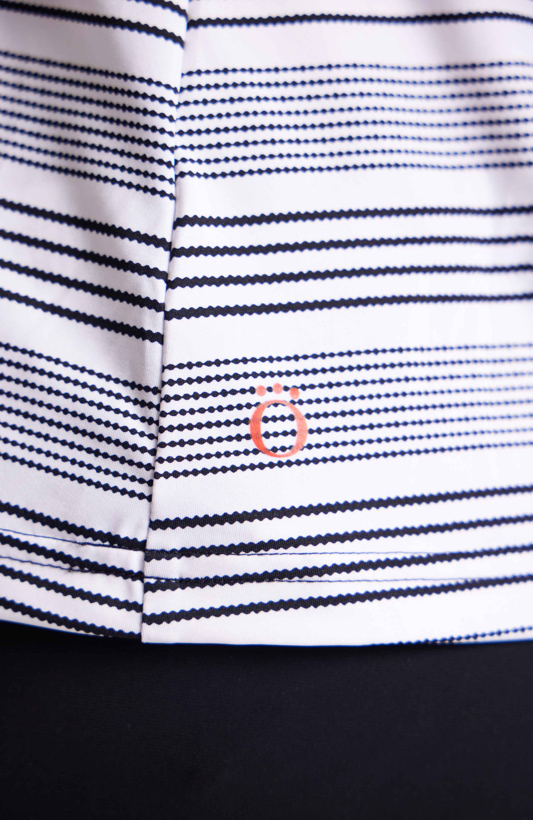 Red KINONA Logo at hem of shirt.  Logo is red circle with 3 solid circles on top