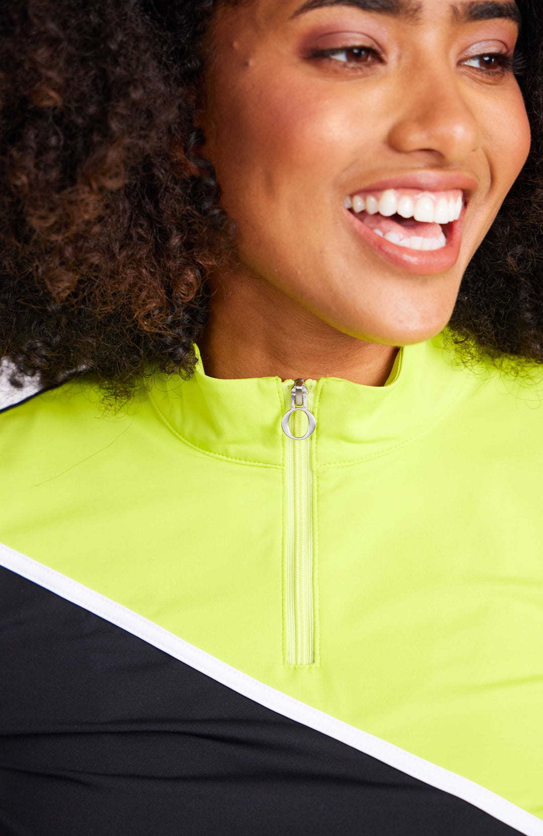 Up close front facing view of woman in a black and chartreuse short sleeve 1/4 zip mock neck top. Top has diagonal thin white stripe across chest