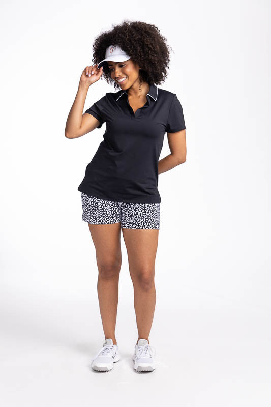 Full front view of a woman wearing the Carry My Cargo Golf Shorts in Fall Bloom print, the Classic and Fantastic Short Sleeve Golf Top in black, and the No Hat Hair Visor in white.