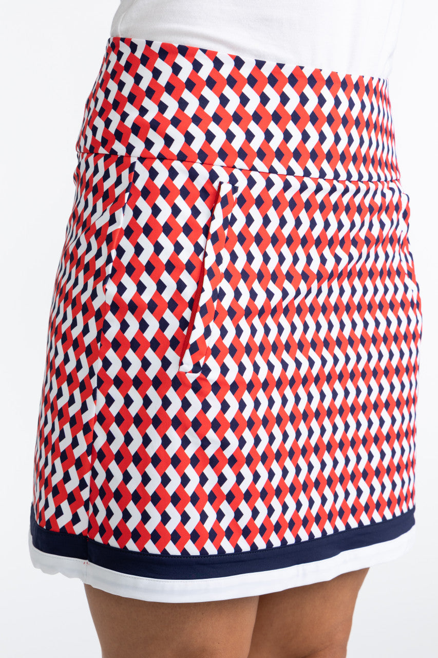 Close right side view of the On The Fringe Golf Skort in Chevron Tomato Red. This pattern consists of red, white, and blue chevrons with two solid stripes at the bottom of the skort - a solid navy blue stripe and a solid white stripe.