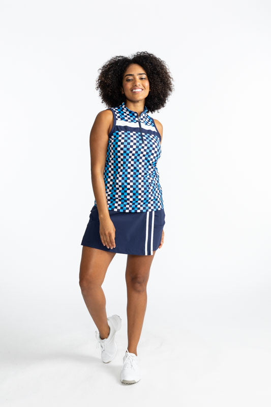Smiling woman golfer wearing the On Target Sleeveless Golf Top in Check It Out (a French Blue, navy blue, and white checked print with a white stripe and a navy blue stripe across the upper chest), and the Skort and Short Golf Skort in Navy Blue and White