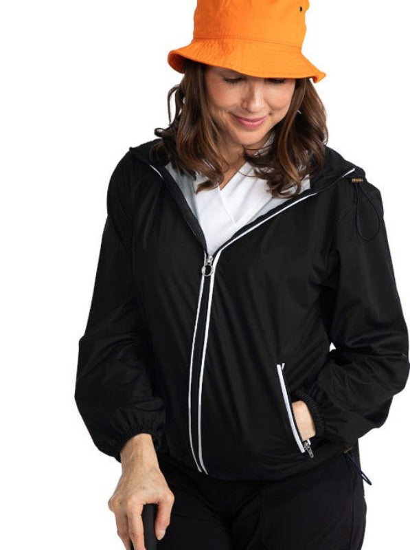 Front view of a woman golfer wearing an orange hat and the Pack and Play Lightweight Golf Jacket in Black.