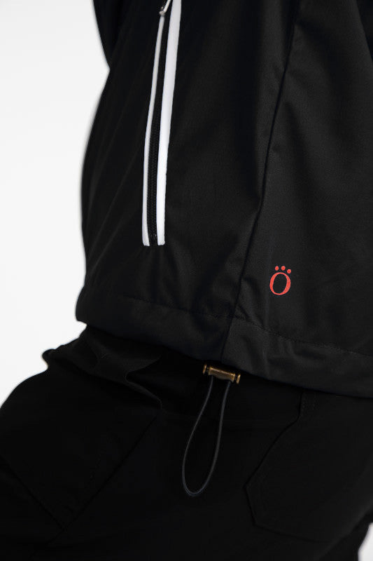 Close front and left side view of the hemline and the adjustable drawstrings on the Pack and Play Lightweight Golf Jacket in Black.