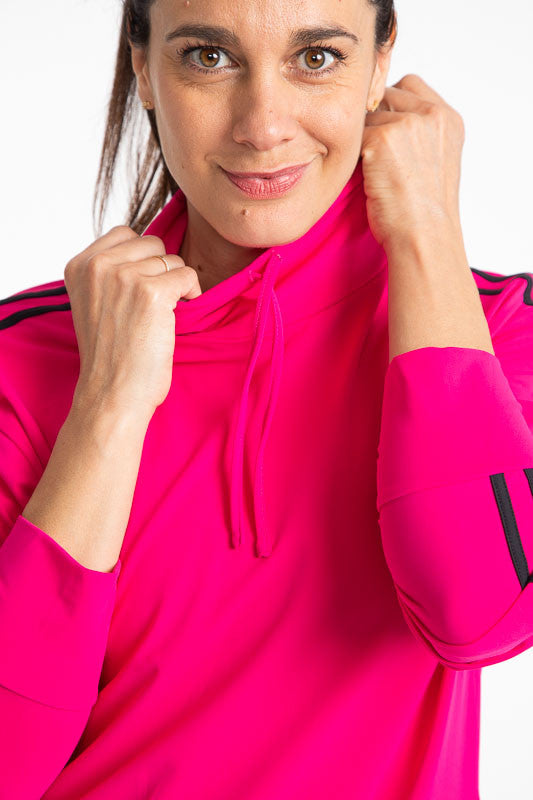 Smiling woman golfer wearing the Apres 18 Funnel Neck Long Sleeve Top in Magenta Pink. This top has two black stripes running down each arm and magenta pink drawstrings around the neck and waistband.