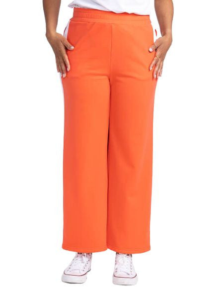 Front view of the Aprés 18 Wide Leg Pants in Coral Red. These are a solid coral red pants with one white stripe up each leg.