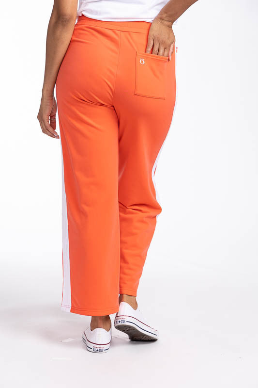 Back view of the Aprés 18 Wide Leg Pants in Coral Red. These are a solid coral red pants with one white stripe up each leg.