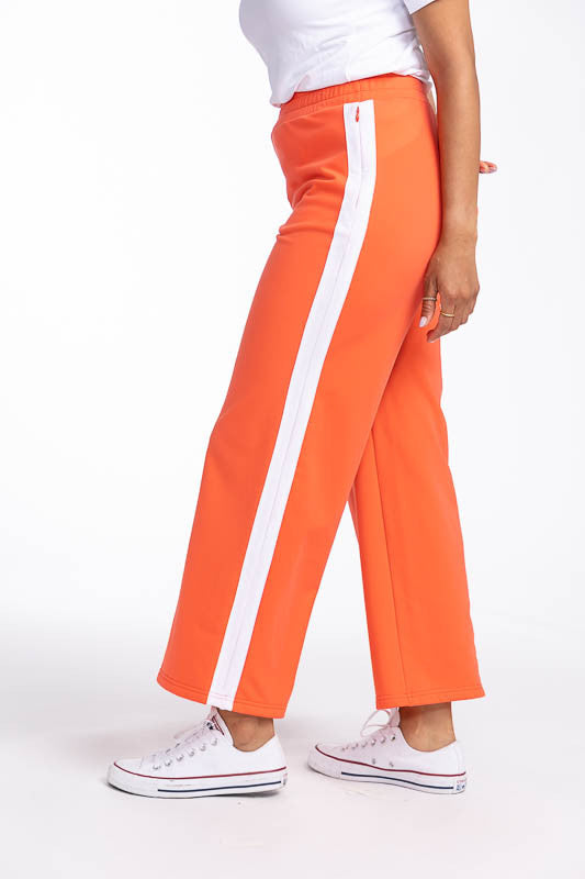 Left side view showing the white stripe up the leg on the Aprés 18 Wide Leg Pants in Coral Red. These are a solid coral red pants with one white stripe up each leg.