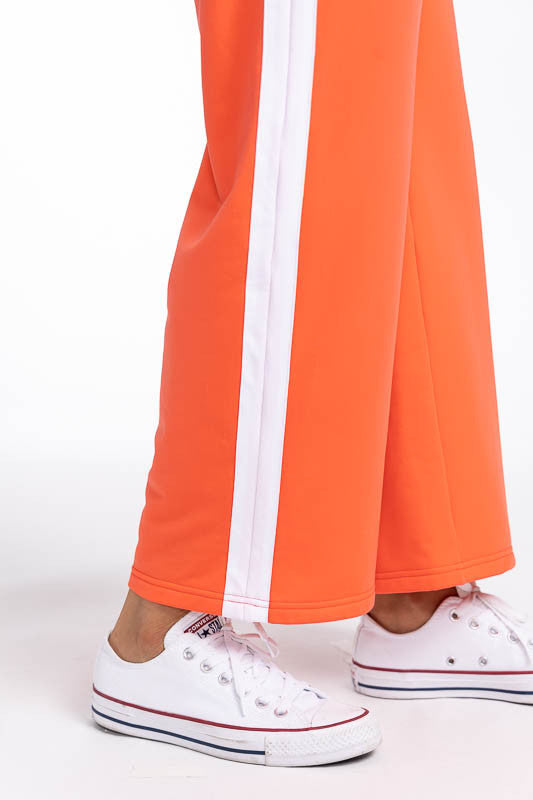 Close right side view of the hemline on the Aprés 18 Wide Leg Pants in Coral Red. These are a solid coral red pants with one white stripe up each leg.