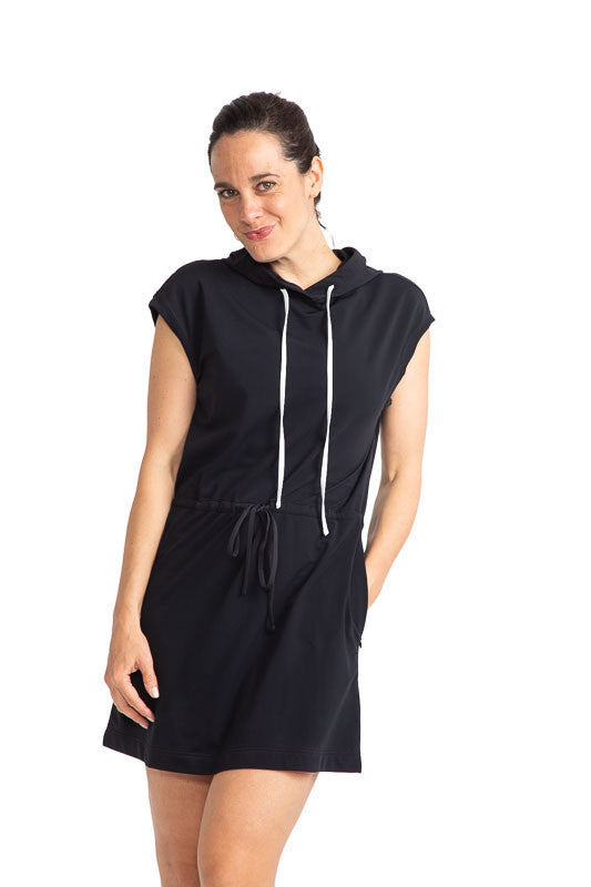 Front view of a woman wearing the Apres 18 Hoodie Dress in Black. This hoodie dress has white drawstrings at the hood and a black drawstring at the waistline.