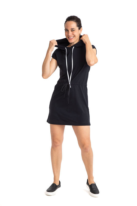 Full front view of a woman wearing the Apres 18 Hoodie Dress in Black. This hoodie dress has white drawstrings at the hood and a black drawstring at the waistline.