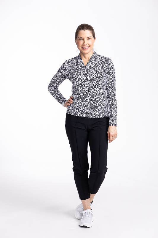 Full front view of a smiling woman wearing the Lovely Layer Long Sleeve Golf Top in Fall Bloom print and the Tailored Crop Golf Pants in Black.
