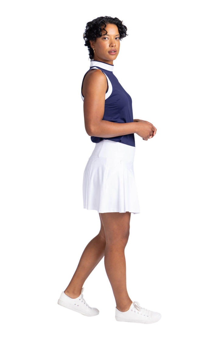 Full side view of a woman wearing the Knock Out top in navy blue; a sleeveless top with white contract panels on the armholes and around the neckline. 