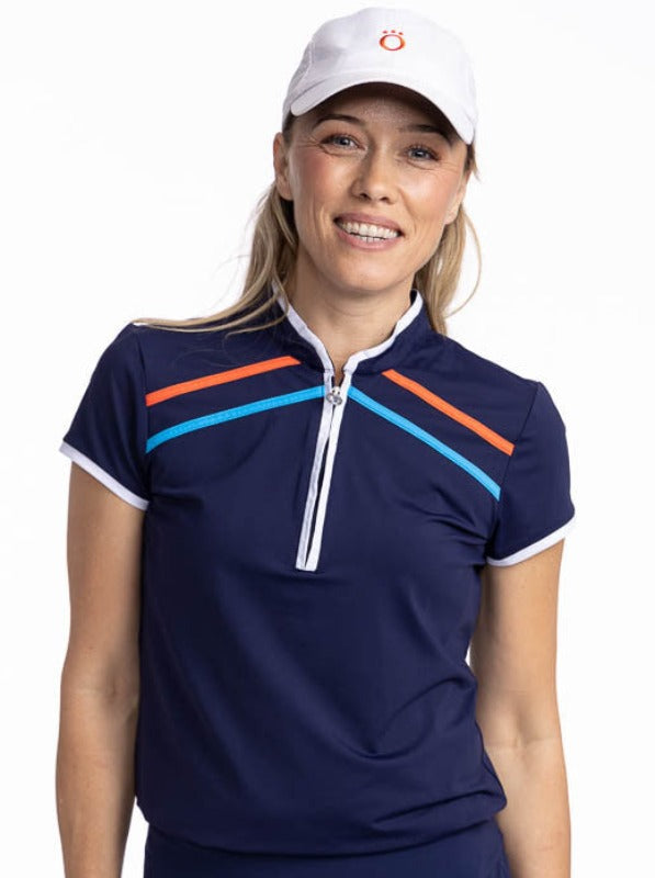Close front view of a smiling woman wearing the Gimme Putt Short Sleeve Golf Top in Navy Blue and the We've Got You Covered Hat in White. The Gimme Putt top is a solid navy blue top with  two diagonal stripes on either side of the front quarter zip - one 