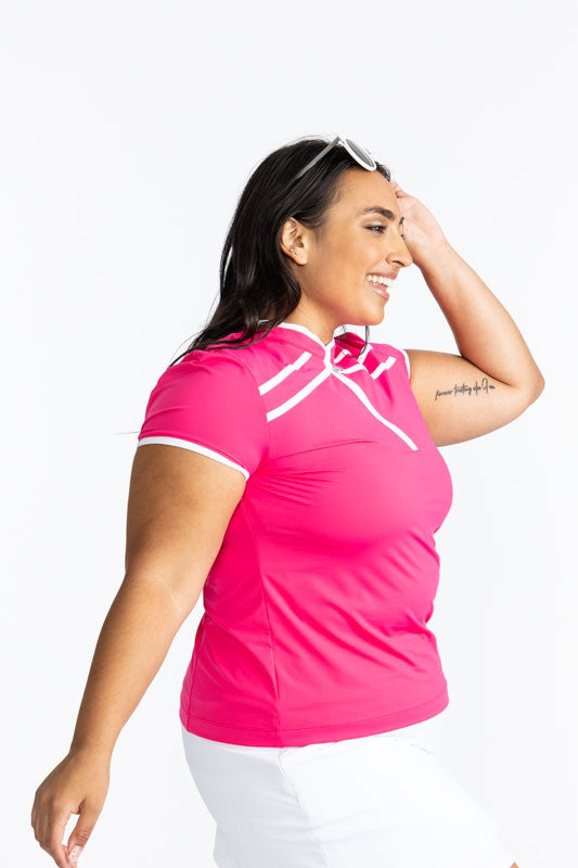 Right side view of a smiling woman with sunglasses on her head wearing the Gimme Putt Short Sleeve Golf Top in Preppy Pink.  This is a solid pink top with a white 1/4 zip front, white trim around the sleeves, and two sets of white, angled stripes below th