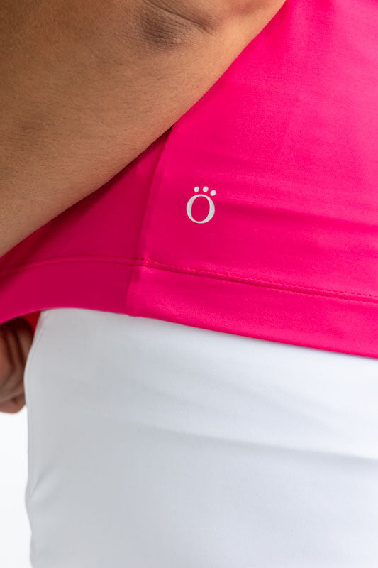 Close left side and back view of the hemline on the Gimme Putt Short Sleeve Golf Top in Preppy Pink.  This is a solid pink top with a white 1/4 zip front, white trim around the sleeves, and two sets of white, angled stripes below the shoulders.
