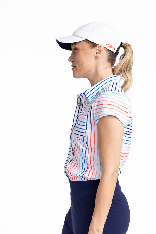 Left side view of the Tough in the Rough Short Sleeve Golf Top in Sun Stripe print and the We've Got You Covered Hat in White. The Sun Stripe print consists of a mix of horizontal and vertical stripes in coral red, pacific blue, and navy blue on a white b