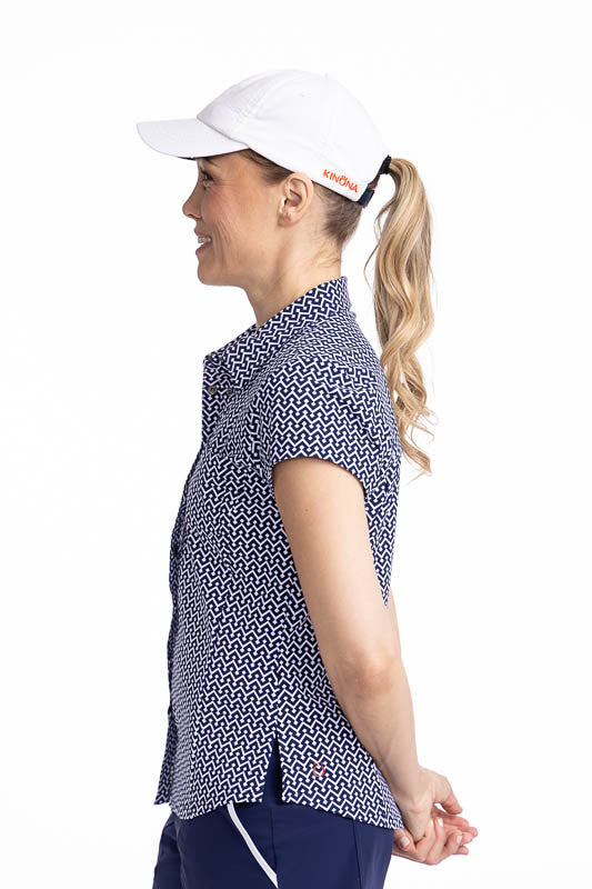Left side view of the Tough in the Rough Short Sleeve Golf Top in Chic Chevron print and the We've Got You Covered Hat in White. The Chic Chevron print consists of white chevrons on a navy blue background. The top features a snap front closure, shirt-styl