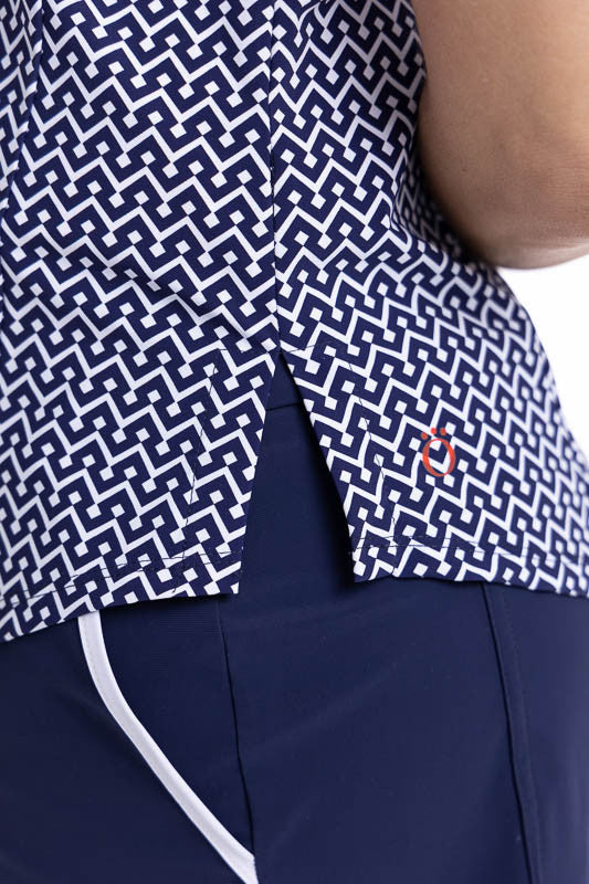 Close right side view of the hemline on the Tough in the Rough Short Sleeve Golf Top in Chic Chevron print and the We've Got You Covered Hat in White. The Chic Chevron print consists of white chevrons on a navy blue background. The top features a snap fro