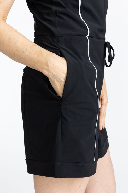 Close right side view of the pocket and hemline on the Style for Miles Sleeveless Golf Romper in Black. This is a solid black piece with white trim around each armhole and one thin, white stripe that runs down each side.