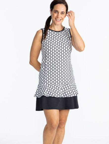 Front view of a smiling woman wearing the On In Two Sleeveless Golf Dress in Spiral Floral print. This is a retro style black and white print with a large, solid black section at the base of the dress.