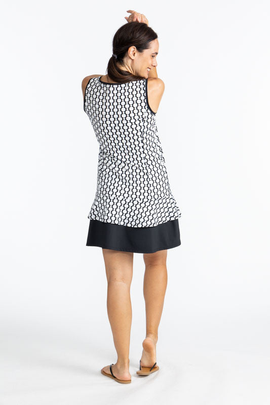 Full back view of a woman wearing the On In Two Sleeveless Golf Dress in Spiral Floral print. This is a retro style black and white print with a large, solid black section at the base of the dress.