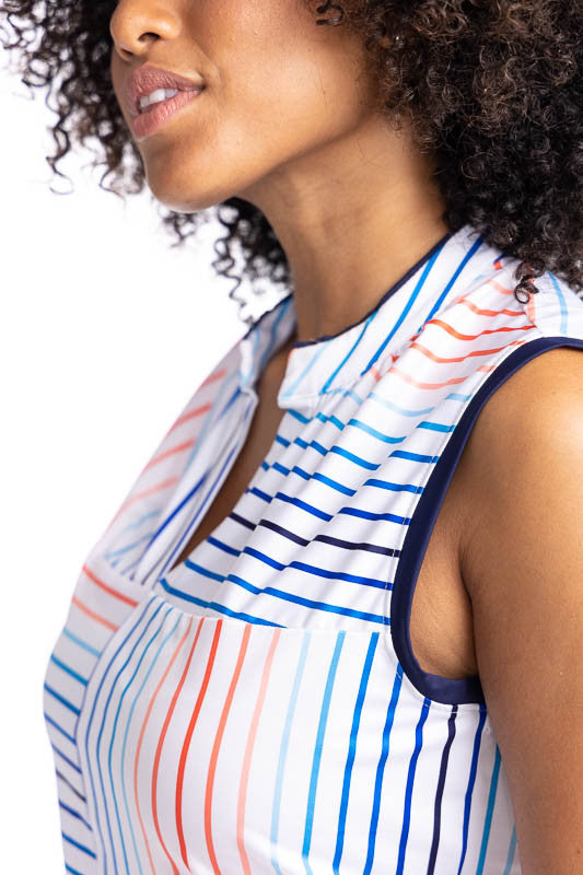 Close front and left side view of the neckline and armhole on the Sandy Par Sleeveless Golf Top in Sun Stripe Print and the No Hat Hair Visor in White. The print consists of a mix of horizontal and vertical stripes in coral red, pacific blue, and navy blu