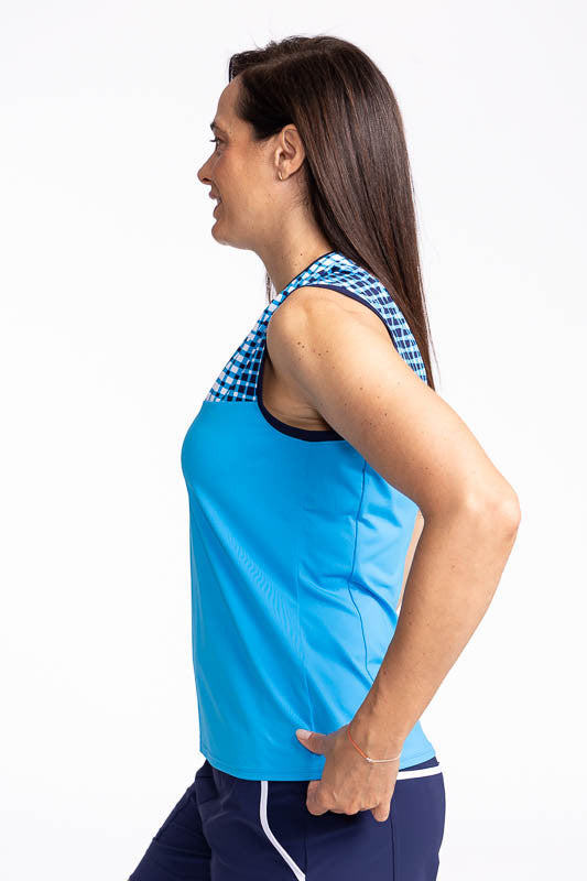 Left side view of the Sandy Par Sleeveless Golf Top in Pacific Blue. This top has the top quarter of the top in Ocean Plaid print and the remaining 3/4 in solid Pacific Blue. The Ocean Plaid print is is a repeating gradient of white to blue checkered prin