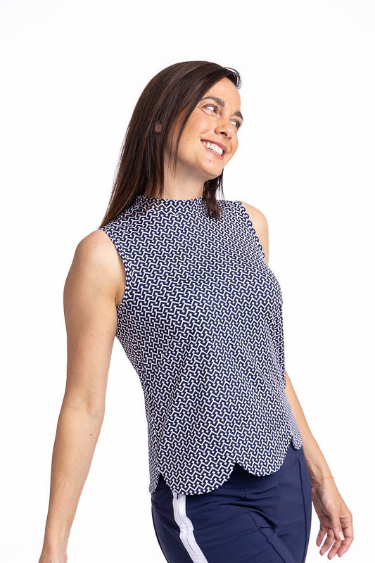 Front view of a smiling woman wearing the On The Edge Sleeveless Golf Top in Chic Chevron print. This is a white chevron print on a blue background. This top features a back zipper and a feminine scallop design along the hemline.